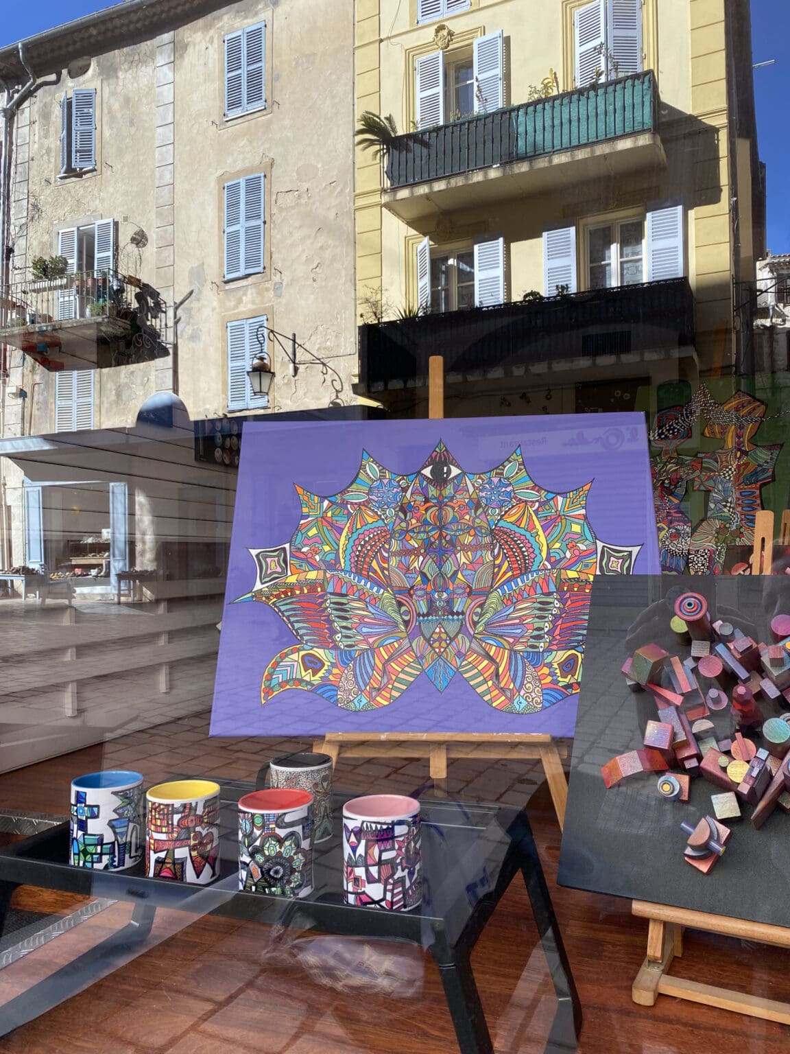Contemporary art display at Galerie Joie De Vivre with a painting on canvas, custom art mugs on a small table, and a block sculpture on a wooden canvas.